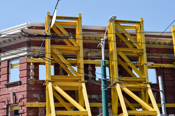 Naklejka premium Yellow steel facade retention towers supporting the historic exterior walls of a heritage building during redevelopment at 378 Queen Street West in downtown Toronto, May 2026