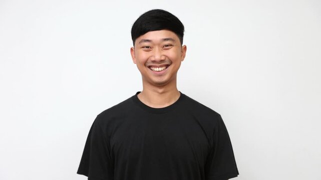 young Asian man in a plain black t-shirt smiles widely and happily against a crisp white background