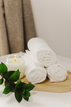 Minimalist still life of luxury spa essentials. White cotton towels with soy wax candle on a table.