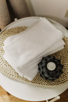 Minimalist still life of luxury spa essentials. White cotton towels with decorative candle on a table.