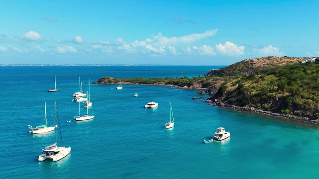Drone view of sailboats and catamarans anchored in a calm tropical bay near Friar's Bay Beach on Saint Martin island. The turquoise ocean waters surround the lush green coastline of the French side.