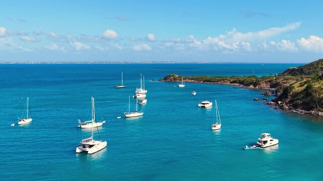 Drone view of sailboats and catamarans anchored in a calm tropical bay near Friar's Bay Beach on Saint Martin island. The turquoise ocean waters surround the lush green coastline of the French side.