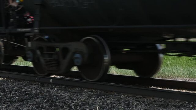Close-up of train wheels moving along tracks with sunlight below the train
