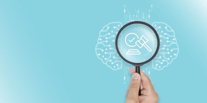 Magnifying glass focusing on law icon and gavel for legal AI compliance. Human hand holding lens over artificial intelligence brain background for judicial auditing and regulation technology.