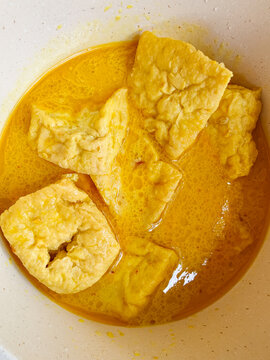 Close up view of traditional Indonesian gulai tahu cooked in rich yellow coconut milk curry sauce inside a pot