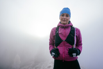 Fototapeta premium Confident female hiker in a pink jacket standing still on a misty mountain summit.Female Hiker Standing on Misty Peak