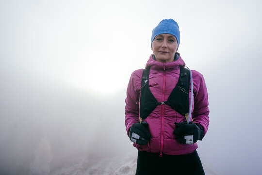 Confident female hiker in a pink jacket standing still on a misty mountain summit.Female Hiker Standing on Misty Peak