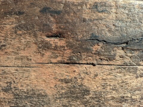 a close-up view of an old, weathered wooden surface with a rich, dark brown color and prominent rustic textures. The wood features distinct horizontal cracks, deep grain lines