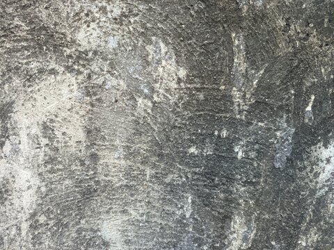 An old weathered concrete wall with a rough and porous texture. A large portion of the surface is covered in dark mold stains and patches of moss.