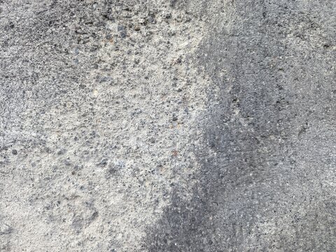 An old weathered concrete wall with a rough and porous texture. A large portion of the surface is covered in dark mold stains and patches of moss.