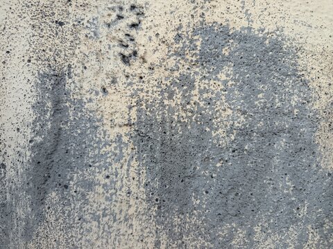 An old weathered concrete wall with a rough and porous texture. A large portion of the surface is covered in dark mold stains and patches of moss.