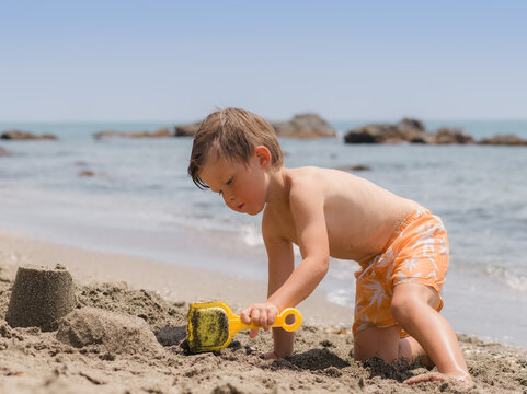 Child Builds Sandcastles on Beach by the Ocean in Sunny Weather