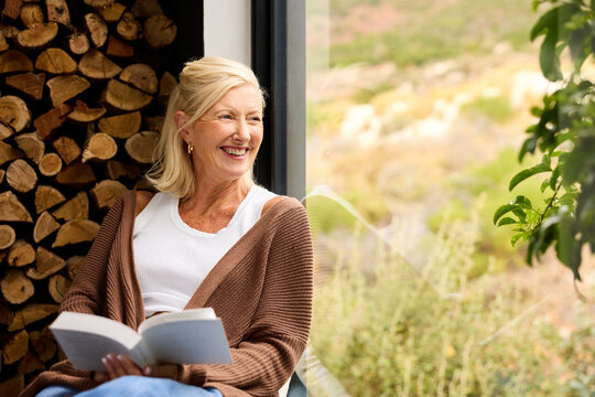 Woman Reading a Book by Window With Stacked Wood