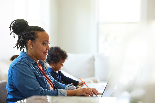 Woman Working on Computer While Child Draws Nearby