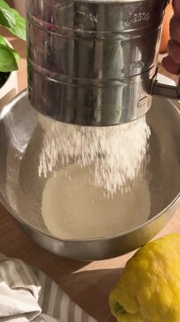 Sifting flour with a sifter into a metal bowl for baking