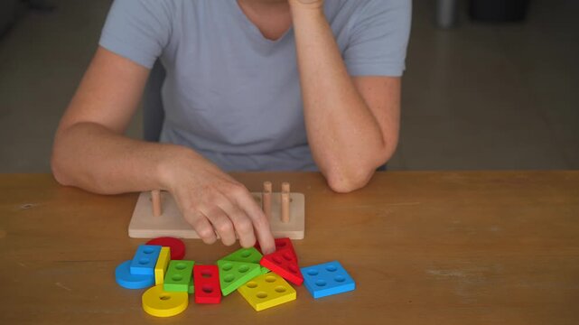 Woman assembling a wooden shape sorter toy at a table, high quality audio recording. Gentle clicking and moving sounds of wooden pieces. Play, learning, and everyday lifestyle concept.