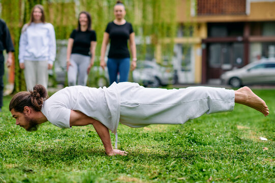 Man Performing Advanced Yoga Balance Pose Outdoors in Park During Group Training Session