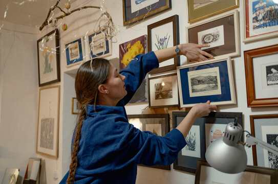 A female artist hangs paintings on the wall