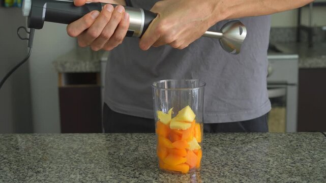 Close up man making fruit smoothie with hand blender with clear sound. Hands blending fresh ingredients in glass. Healthy drink preparation, kitchen routine and ASMR concept.