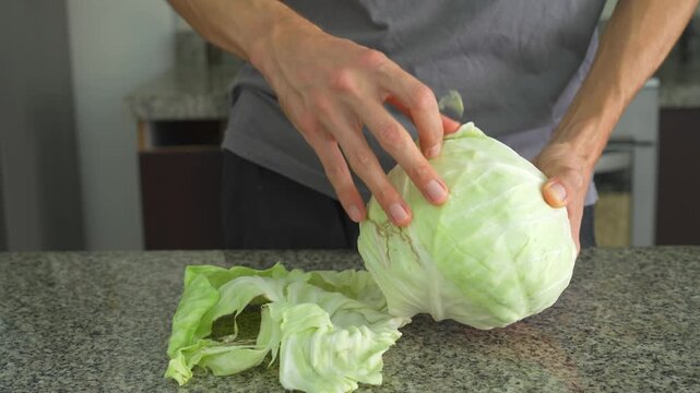 Close up man peeling cabbage leaves with clear sound. Hands preparing fresh vegetable at table. Cooking prep, healthy food, kitchen routine and ASMR concept.