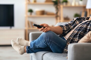 Obraz premium Person relaxing on couch holding TV remote, watching television at home