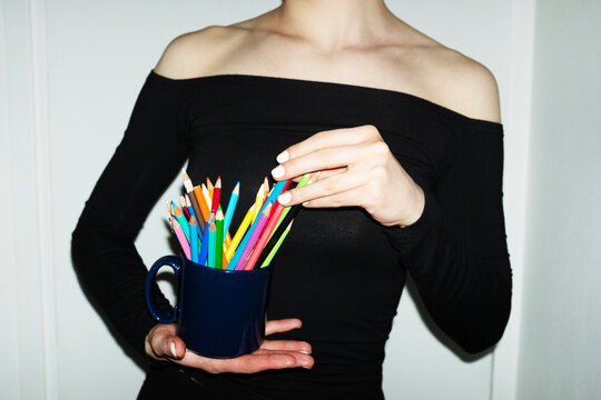Person holding a coffee cup full of colourful art drawing pencils 