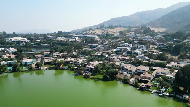 Aerial panning shot over the wealthy residential neighborhood of La Planicie, showcasing upscale architectural designs, private pools, and the unique landscape of La Molina, Peru.