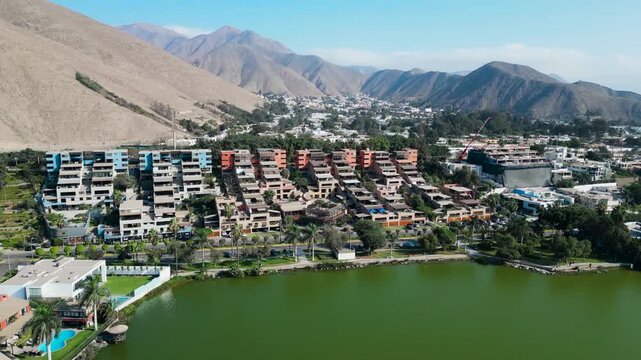 Drone tracking shot focusing on the unique multi tiered terracotta colored luxury residential complex built into the dry mountainside overlooking the La Planicie lagoon in La Molina.
