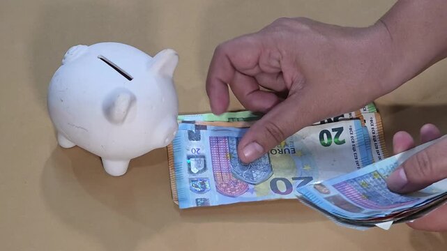 Hands counting euro banknotes next to white piggy bank, close up view