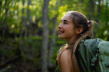 Fototapeta premium Portrait of confident female hiker enjoying an active day outdoors surrounded by lush green forest nature. Concept of travel, happiness and connection with the natural world.