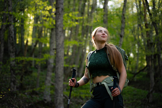 Female backpacker exploring woodland trails and enjoying a peaceful moment in nature. Portrait of a woman hiker in the woods with a copy space. The concept of travel, adventure, and well-being.