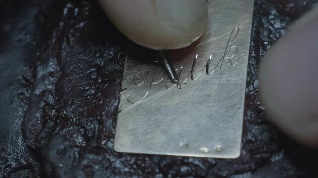 Hand engraving elegant cursive script letters into gold jewelry pendant closeup macro detail