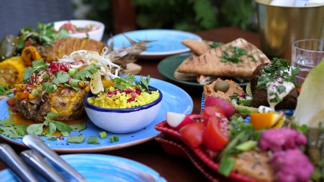 Colorful and vibrant vegan feast featuring a variety of middle eastern dishes, including falafel, hummus, fresh vegetables, grilled pineapple, and couscous, beautifully arranged on a wooden table