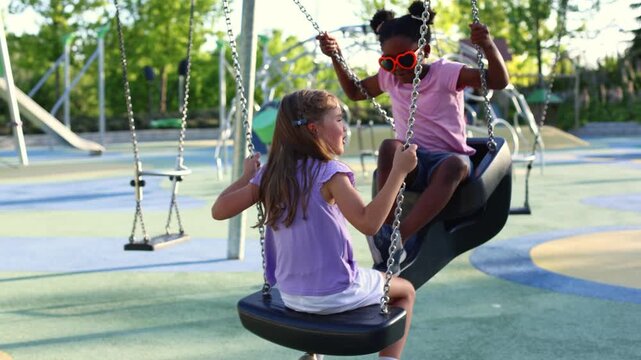 Two little girls playing together on a swing at the park