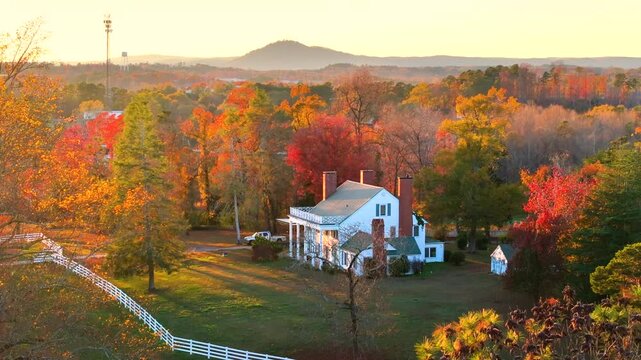 Elegant farmhouses hidden between bright autumn trees, golden leaves framing property in peaceful southern rural scene.