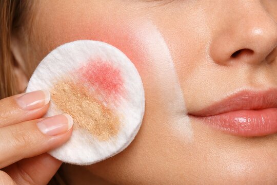 Woman using cotton pad to remove makeup from cheek. Face skin cleaning concept. Daily skincare routine for healthy complexion. Beauty process with cosmetic product and hygiene accessory.