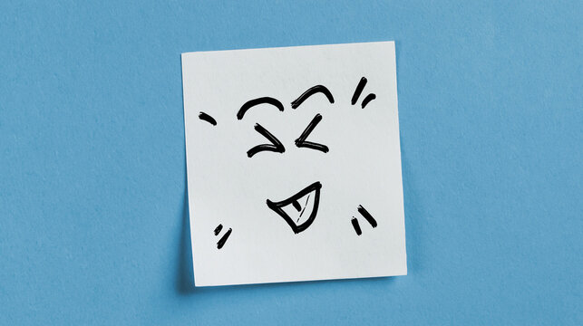 Smiley face doodle on sticky note against blue background. Sticky note with hand-drawn emoj
