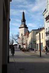 Obraz premium Church tower and pedestrian street scene in small Polish town on sunny day