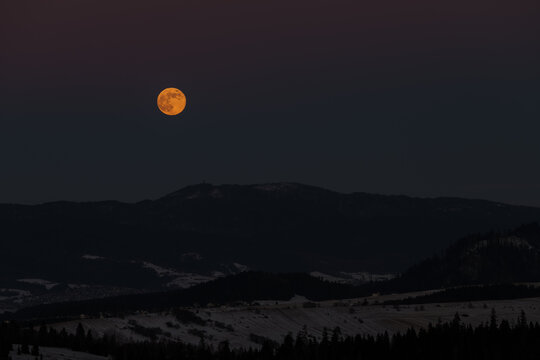 Full moon rising over mountain ridge at twilight. Beautiful orange supermoon in dark dusk sky