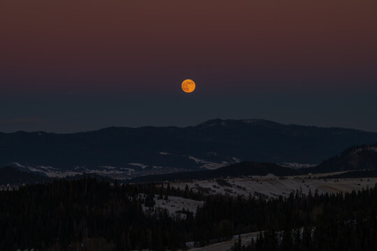 Full moon rising over mountain ridge at twilight. Beautiful orange supermoon in dark dusk sky
