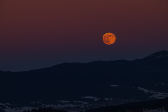 Full moon rising over mountain ridge at twilight. Beautiful orange supermoon in dark dusk sky