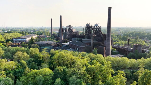 Eine beeindruckende Luftaufnahme des Landschaftsparks Duisburg-Nord zeigt die stillgelegten Hoch&ouml;fen und Schornsteine des alten H&uuml;ttenwerks, umgeben von dichten, gr&uuml;nen Baumkronen.