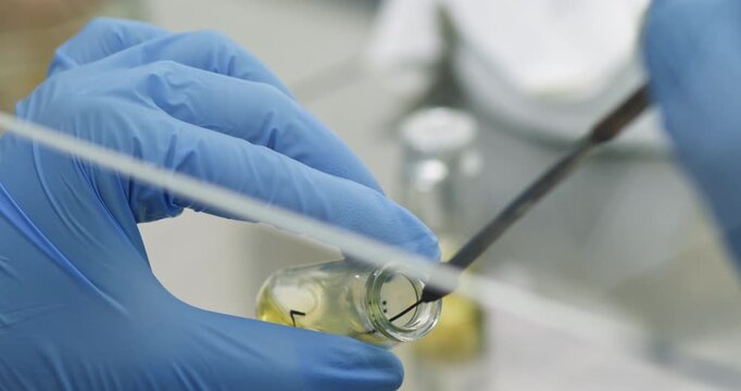 A scientist added bacteria to a liquid in a flask using a microbiological loop and is vigorously shaking the loop in the liquid, close-up.