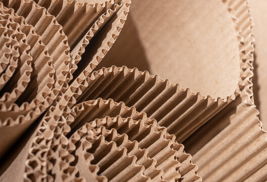Extreme close-up of corrugated cardboard rolls with repeating wavy fluting pattern in warm brown tones. Eco-friendly recycled kraft paper packaging material, abstract geometric