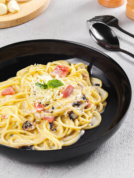 Creamy Carbonara Pasta with Bacon and Parmesan Cheese in Black Plate, Italian Spaghetti with White Cream Sauce and Fresh Parsley Garnish