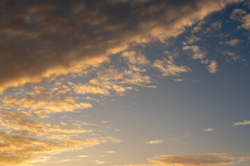 Fototapeta premium Sunset sky background with a band of golden orange altocumulus clouds across a blue sky. Warm dramatic cloudscape, nature background..
