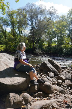 senior woman sitting on a rock by kabir kouba river
