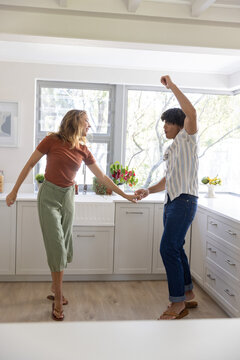 Couple holding hands and dancing in sunlit kitchen in casual outfits by farmhouse sink