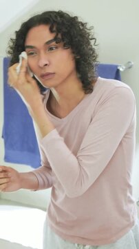 Vertical video: Leaning person in pink top pressing cotton pad at bathroom mirror, removing makeup