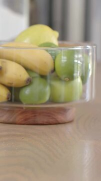 Vertical video: Moving camera inching, highlighting glass bowl with bananas and apples on table